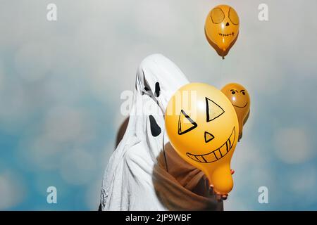 Frohe Halloween. Geister umarmen sich. Kinder in weißen Kostümen und bemalten orangefarbenen Kugeln auf blau schimmerndem Hintergrund. Verschiedene Emotionen der Freude, Wut. Festliche Dekoration, Konzept der Party zu Hause. Stockfoto