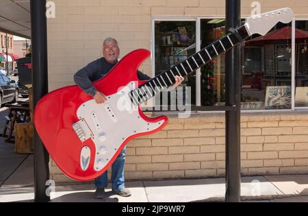Ein älterer Herr, der vorgibt, eine sehr große vorgeblich vorgebende Gitarre an der Straßenecke von Winslow, Arizona, zu spielen. Stockfoto