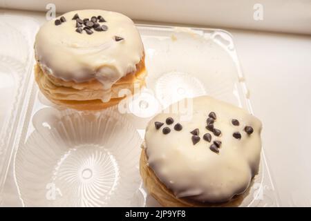 Zwei leckere Donuts mit Puderzucker und Schokoladenstückchen auf weißem Hintergrund in einem transparenten Kunststoffbehälter Stockfoto