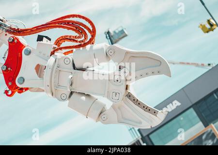 Weißer offener Roboterarm mit orangefarbenen und roten Details über einem blauen Himmel und einem Gebäude Stockfoto