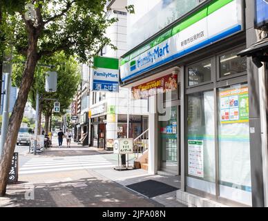 Die Schaufensterfront schoss an einem hellen sonnigen Sommernachmittag von einem belebten schattigen Bürgersteig eines FamilyMart, einem beliebten japanischen Lebensmittelladen. Stockfoto