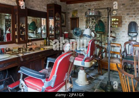 Interieur des 20.. Jahrhunderts Barbershop / Friseur / Friseursalon mit Vintage-Ausrüstung und antiken Barbierstühlen, Museum Bachten de Kupe, Belgien Stockfoto