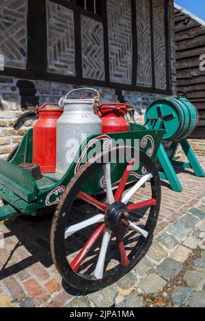 Antiker Handwagen, beladen mit vier alten Metall-Milchkännern / Milchdosen und Vintage-Holzfass-Butter-Churn Stockfoto