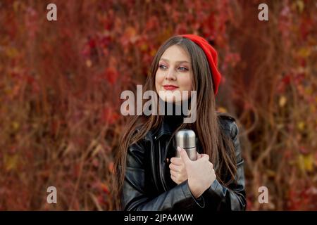 Schöne stilvolle junge Frau in schwarzer Lederjacke stehen und posieren im Herbst Park auf rotem Hintergrund Blätter Stockfoto