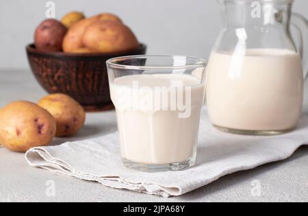 Vegane Kartoffelmilch im Glas und im Krug auf hellgrauem Tisch. Verwendung von pflanzlicher und laktosefreier Milchaustauschmaschine Stockfoto