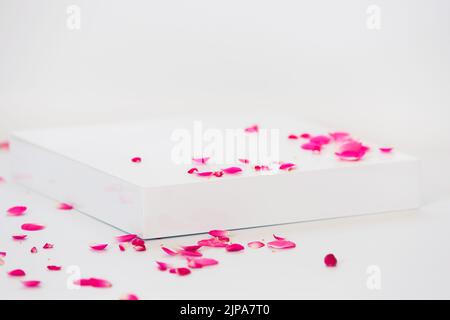 Leeres Podium mit Rosenblüten auf weißem Hintergrund. Abstrakter Hintergrund für Produktpräsentation, Geschenk oder Kosmetik Stockfoto