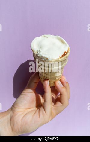 Hand hält einen Eiskegel auf dem violetten Hintergrund. Stockfoto
