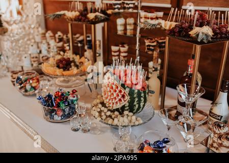 Stilvolle Desserts mit Erdbeere, Süßigkeitenbar mit Süßigkeiten bei einem luxuriösen Hochzeitsempfang. Catering im Restaurant. Cupcakes Makronen auf dem Tisch. Platz für Stockfoto