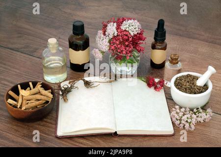 Baldrian Kräuterwurzel und ashwagandha Ginseng Kräuterpflanzenmedizin mit Notizbuch, ätherische Ölflaschen. Natürliche adaptogen pflanzliche Heilmittel. Stockfoto