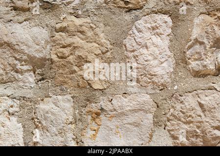 Fragment einer Wand aus einem abgebrochenen Stein. Beige und weiße Kopfsteinpflaster in verschiedenen Größen, Hintergrund, Textur. Stockfoto