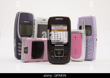 Eine Gruppe von Retro-Handys, Motorola, Nokia, Samsung, Sagem. Fotografiert auf weißem Hintergrund. Die Telefone zeigen Markierungen aus der Verwendung an.
