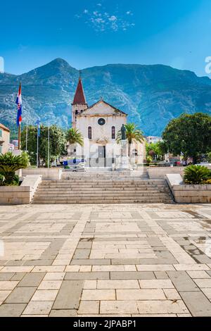 Kathedrale und Kirche des Heiligen Marko in Makarska, Kroatien. Im Hintergrund das Biokovo-Gebirge. Sonniger Tag im Sommer, grüne Bäume an der Seite. Dal Stockfoto
