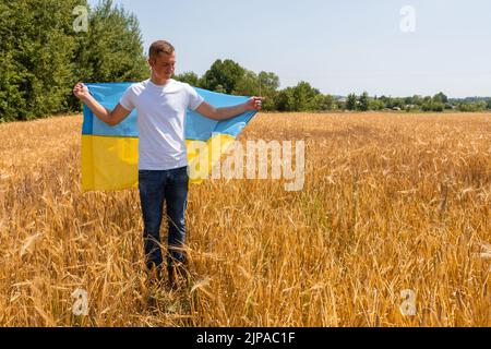 Hübscher Junge mit gelb-blauer Flagge der Ukraine im Weizenfeld. Friedenskonzept Stockfoto