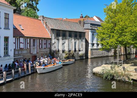 Brügge, Belgien - 2022. August: Menschen steigen in ein Motorboot für eine Reise rund um das Kanalsystem der Stadt Stockfoto