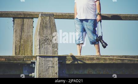 Ein Blick auf einen Fotografen, der alleine mit einer Kamera auf dem Pier läuft Stockfoto