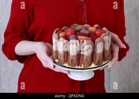 Die Frau hält einen französischen charlotte-Kuchen mit Sommerfrüchten in der Hand. Party-Dessert Stockfoto