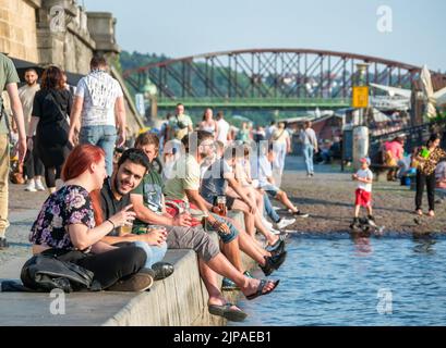 Prag, Tschechische Republik - 2022. Juni: Touristen und Einheimische sitzen und trinken ein Bier auf der Naplavka entlang der Moldau in Prag Stockfoto