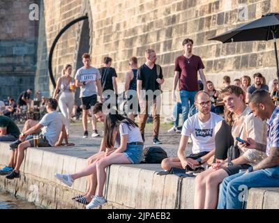 Prag, Tschechische Republik - 2022. Juni: Touristen und Einheimische sitzen und trinken ein Bier auf der Naplavka entlang der Moldau in Prag Stockfoto