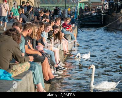 Prag, Tschechische Republik - 2022. Juni: Touristen und Einheimische sitzen und trinken ein Bier auf der Naplavka entlang der Moldau in Prag Stockfoto