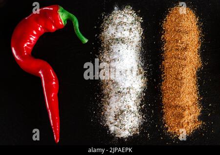 Chilischoten, Salz, Gewürze, Vansalz und Gewürze liegen auf dem schwarzen Stein Stockfoto