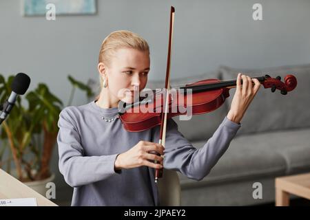 Porträt einer blonden jungen Frau, die zu Hause Geige spielt oder im Musikstudio praktiziert, Kopierraum Stockfoto