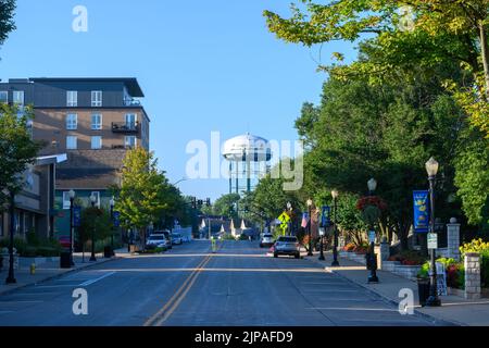 Frühmorgendlicher Blick auf Downers Grove, Illinois Main Street, mit Blick nach Süden auf einen blauen Himmel mit dem Geschäft, den Bäumen und dem Wasserturm der Stadt. Stockfoto