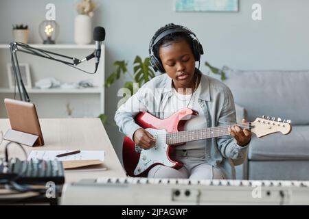 Porträt einer jungen schwarzen Frau, die E-Gitarre spielt und Songs im Heimstudio aufnimmt, Kopierraum Stockfoto