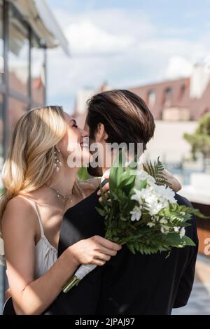 Glückliche Braut hält Bouquet und küssen Freund auf der Terrasse des Restaurants Stockfoto