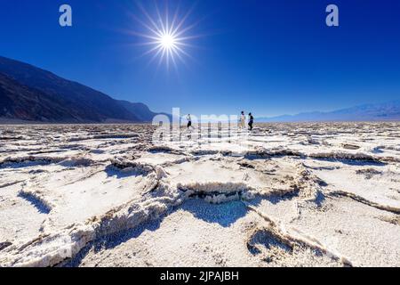 Familie, die an einem sehr sonnigen, klaren Tag über trockene Salzkrusten im Bad Water Basin spazierengeht, Bad Water Basin, Death Valley National Park, Kalifornien Stockfoto