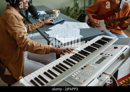 Nahaufnahme einer schwarzen jungen Frau, die die Klaviertasten drückt, während sie mit einer Band junger Musiker Musik komponiert Stockfoto