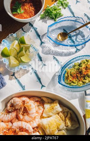 Sommer Meeresfrüchte Abendtisch verteilt, um Fisch Tacos, Garnelen, Guacamole, Limette, Tortilla, Salsa auf blau-weißem Fischtischtuch in der Sonne von Nicole Stockfoto