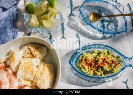 Sommer Meeresfrüchte Abendtisch verteilt, um Fisch Tacos, Garnelen, Guacamole, Limette, Tortilla, Salsa auf blauem und weißem Fischtischtuch in der Sonne Stockfoto