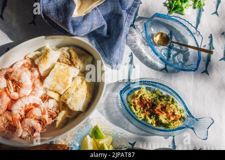 Sommer Meeresfrüchte Abendtisch verteilt, um Fisch Tacos, Garnelen, Guacamole, Limette, Tortilla, Salsa auf blauem und weißem Fischtischtuch in der Sonne Stockfoto