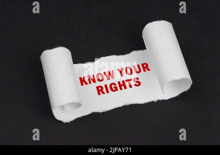 Auf einer schwarzen Oberfläche liegt ein weißes, verdrehtes Papier mit der Aufschrift - Know Your Rights. Bildungskonzept. Stockfoto
