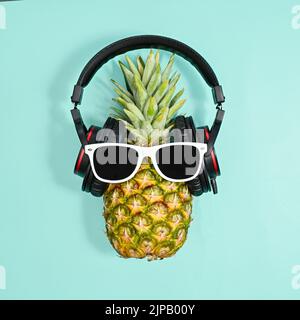Kreative Ananas mit Kopfhörern und Sonnenbrillen auf hellblauem Untergrund. Kreatives Sommerdisco-Konzept. Flach liegend Stockfoto