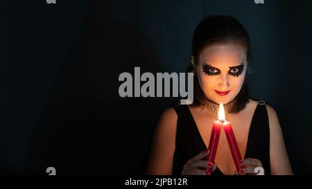 Mädchen im Bild der Hexe schaut direkt in den Rahmen mit brennender Kerze in den Händen auf schwarzem Hintergrund. Konzept von Halloween und Magie. Platz kopieren, Banner Stockfoto