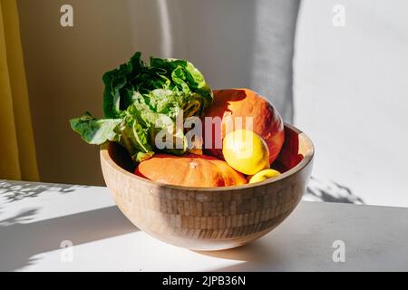 Gemüse - Punpkin, grüner Salat - in einer Bambusschüssel auf weißem Tisch. Tageslicht. Schatten an der Wand. Sonne Licht. Zero Waste Konzept. Kaufen Sie lokale Bio-Lebensmittel ein Stockfoto