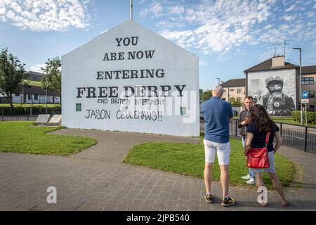 Touristen mit Reiseleiter vor dem Schild, das Free Derry mit einem Wandgemälde von Bogside Artists an der Seite des Hauses in Derry, Nordirland, betreten. Stockfoto
