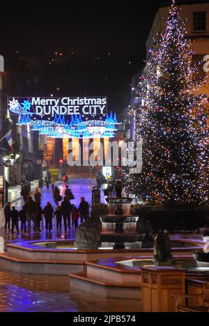 „Merry Christmas Dundee City“, nächtliche Straßenszene mit Weihnachtsbaum, Brunnen und Lichtern, während die Menschen die Reform Street entlang zur High School of Dundee gehen Stockfoto