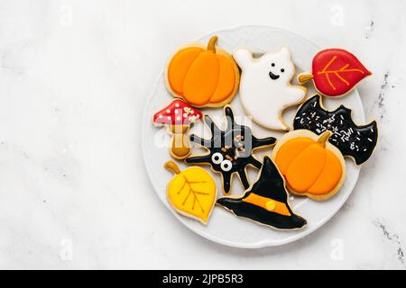 Halloween Zucker Kekse - Kürbis, Geister, Hexenhut, Spinne in einem Teller auf weißem Hintergrund. Draufsicht Stockfoto