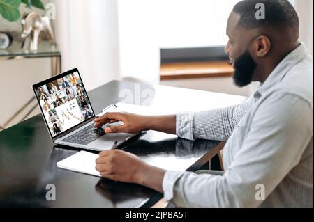 Brainstorming der Finanzgruppe. Intelligenter afroamerikanischer Mann, sitzt an einem Schreibtisch im Büro oder zu Hause, spricht auf einer Videokonferenz mit Kollegen, diskutiert neue Ideen und Finanzplan, Strategie Stockfoto