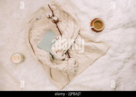 Flache Lay-Szene mit gestricktem warmen Pullover, Kerze und Kaffee auf dem Bett. Winterzubehör, gemütlicher Morgen. Stockfoto