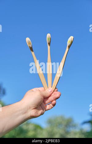 Hand hält drei ökologische Bambus-Zahnbürsten im Freien. Konzepte: Nachhaltiger Lebensstil, Verwendung kompostierbarer und umweltfreundlicher Materialien Stockfoto