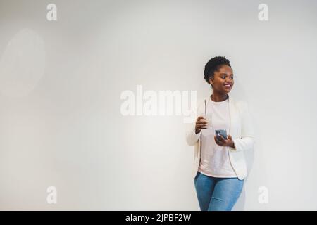 Positive dunkelhäutige Frau genießt die Arbeitspause im Café, trinkt kaltes Getränk und schreibt SMS-Nachrichten auf dem Handy. Lehnt sich an den Stockfoto