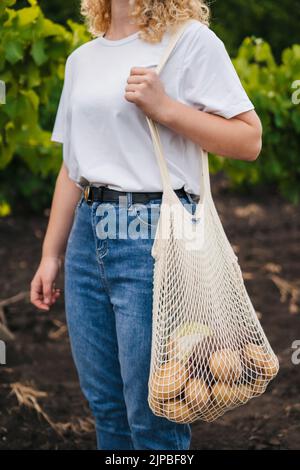 Porträt eines unbekannten Mädchens, das einen Einkaufstasche aus Baumwollstring mit Gemüse hält. Umweltfreundlicher Style. Kein Kunststoff. Stockfoto