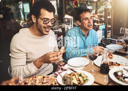 Wo soll ich anfangen? Zwei fröhliche junge Männer sitzen tagsüber an einem Tisch und essen Pizza in einem Restaurant. Stockfoto