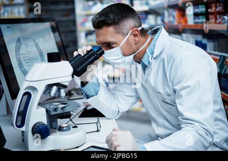 Er entwickelt effektive neue Medikamente. Ein reifer Mann, der ein Mikroskop benutzt, während er pharmazeutische Forschung betreibt. Stockfoto