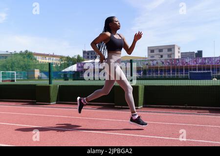 Fit junge schwarze Frau in Sportbekleidung läuft auf der roten Strecke des Stadtstadions Vorbereitung auf Wettbewerbe Stockfoto