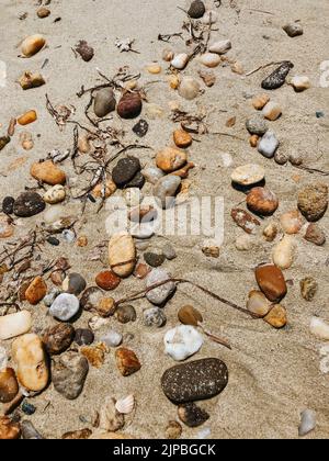 Seesteine am feuchten Sandstrand. Sommer Hintergrund Textur Tapete. Top Luftaufnahme über sonnigen Strandtag. Verschiedene schöne mehrfarbige Runde Stockfoto