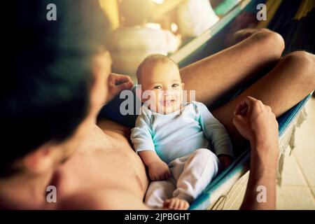 Nichts kann unser Glück wegnehmen. Porträt eines fröhlichen Jungen auf dem Schoß seines Vaters sitzend, während er während des draußen auf die Kamera schaute Stockfoto